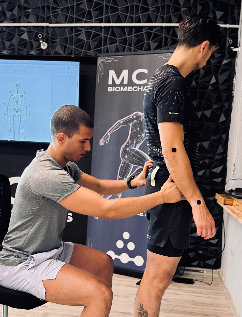 A biomechanics specialist placing motion markers on a man's hip to prepare for a gait and posture analysis.